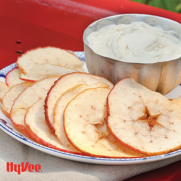 Small bowl of goat cheese dip surrounded by a plate of apple chips
