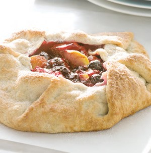 Baked crostata filled with raspberries, blueberries and peaches on parchment paper