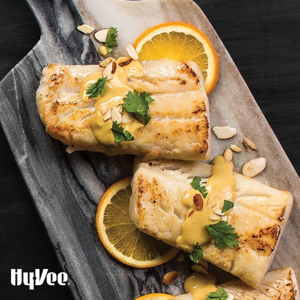 Plate of Cod covered in Citrus-Dijon sauce, Almonds and Cilantro, served with Orange slices