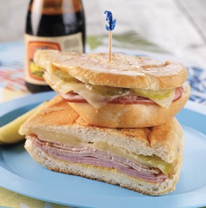 Two Cuban Sandwich halves stacked on a blue plate with a toothpick and pickle