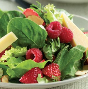 Plate topped with mixed greens, cheese wedges, sliced strawberries, and whole raspberries