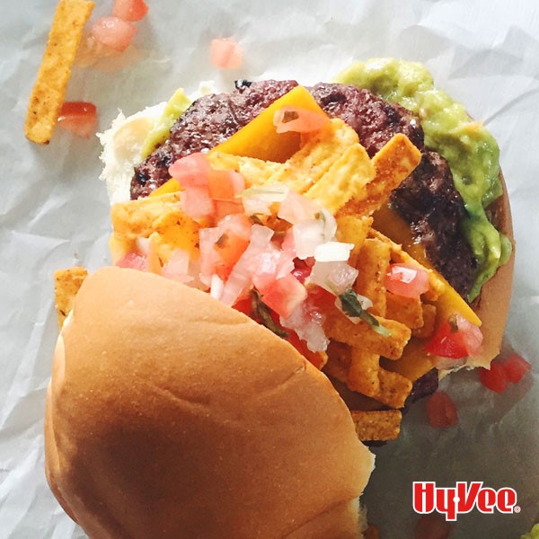 Bun topped with guacamole, burger patty, cheese, corn chips, and pico de gallo.