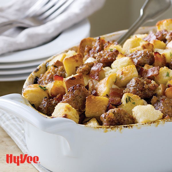 White casserole dish topped with cubed bread, chopped bacon, thyme, and fennel