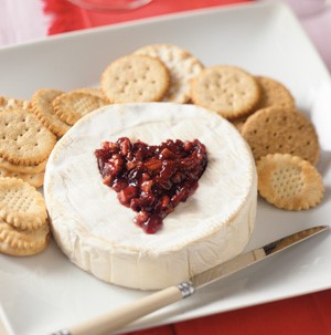 Plate of brie topped with fruit preserve mixture, and served with crackers and a cheese knife 