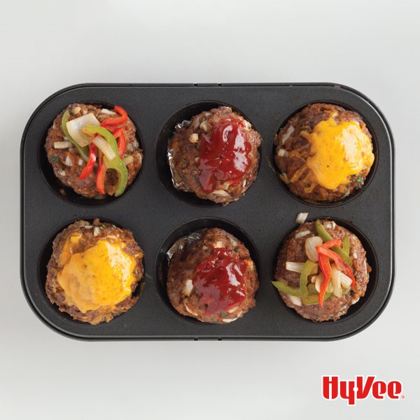 Mini meatloaves in a 6 cup muffin pan topped with cheese, ketchup, and mixed vegetables