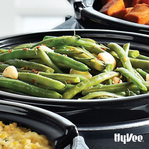 Fresh green beans and garlic cloves on a black plate garnished with red pepper flakes