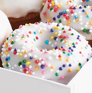 Buttermilk donut topped with white icing and colored sprinkles in a box