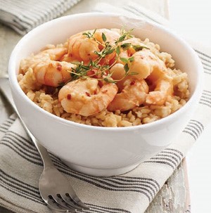 White bowl filled with brown rice, cooked tail-off shrimp, and garnished with fresh thyme
