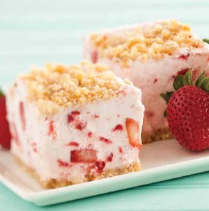 Strawberry cheese cake squares on a plate with crumb topping and whole strawberries