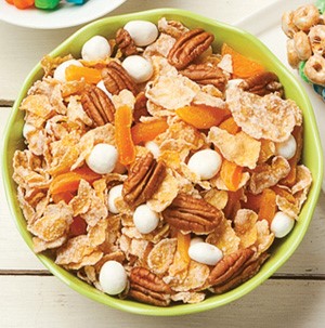 Green bowl filled with flaked corn cereal,mini marshmallows, dried fruit, and pecans