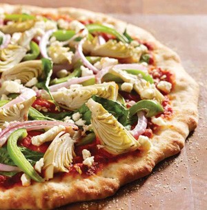 Pizza topped with artichoke hearts, red onion strips, bell pepper strips, and fresh spinach leaves