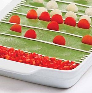 White casserole dish filled with tomato slices, guacamole, and sour cream garnish to look like football field