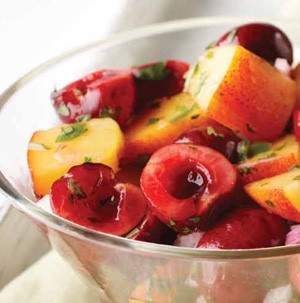 Clear bowl filled with diced peaches, halved cherries, and garnished with fresh chopped herbs