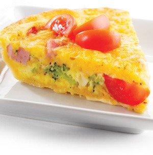 Quiche with chunks of broccoli, ham, and tomatoes on a white square plate