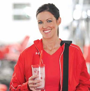 A smiling woman in red holding a strawberry-pineapple smoothie