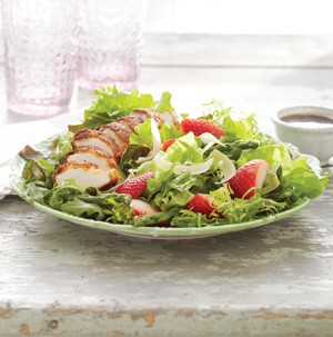 Plate of arugula salad topped with parmesan-crusted chicken, aspargus and strawberries