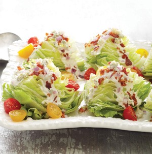 Wedges of lettuce topped with salad dressing, halved red and yellow cherry tomatoes, and chopped cooked bacon