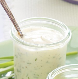 Glass container filled with ranch dressing with a serving spoon