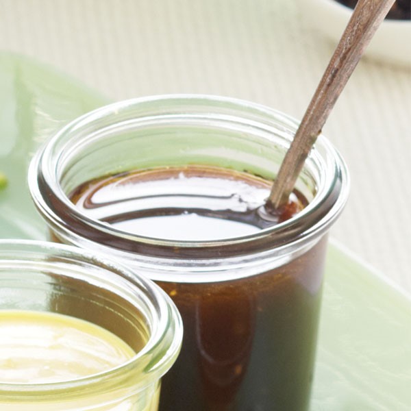 Glass container filled with balsamic vinaigrette with a serving spoon