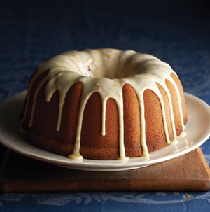 Bundt cake on white plate drizzled dripping with orange zest powdered sugar glaze