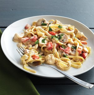 Pasta covered in white sauce with chicken and vegetables on a plate with a fork