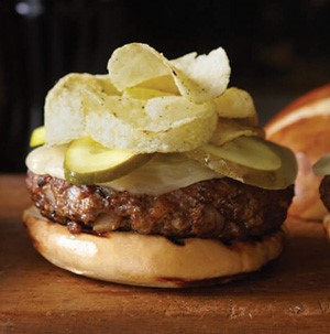 Toasted bun topped with cheeseburger, pickle slices and potato chips
