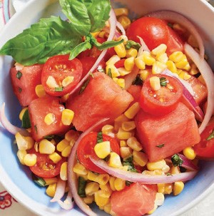 Diced watermelon, corn kernels, sliced red onions and cherry tomatoes in a bowl with basil leaves for garnish