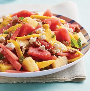 Chopped watermelon and mango salad topped with mint leaves, nuts, and crumbled cheese