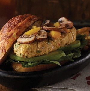 Bun topped with spinach, sliced avocados, quinoa patty, peppers, and mushrooms