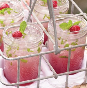 Mason jars filled with pink raspberry mojitos topped with ice, whole raspberry, and fresh mint leaves