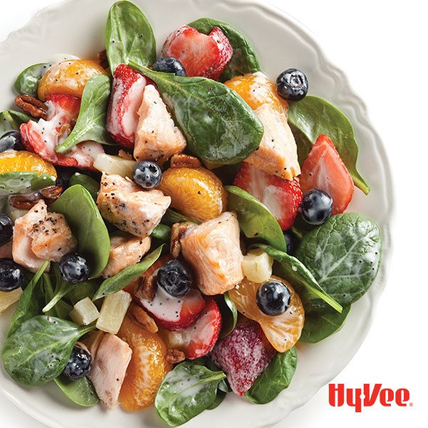 Bowl of spinach salad topped with salmon chunks, mandarin oranges and fresh strawberries and blueberries