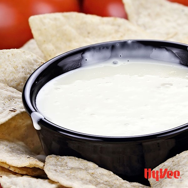 White queso dip in black bowl surrounded by flour tortilla chips