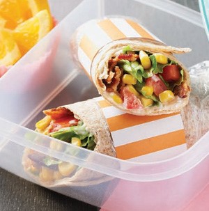 Wraps in a plastic container filled with bacon, corn, chopped tomatoes, and lettuce