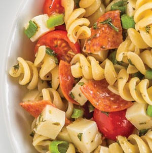 Bowl of pasta salad with pepperoni, pasta, tomatoes, cheese and onions
