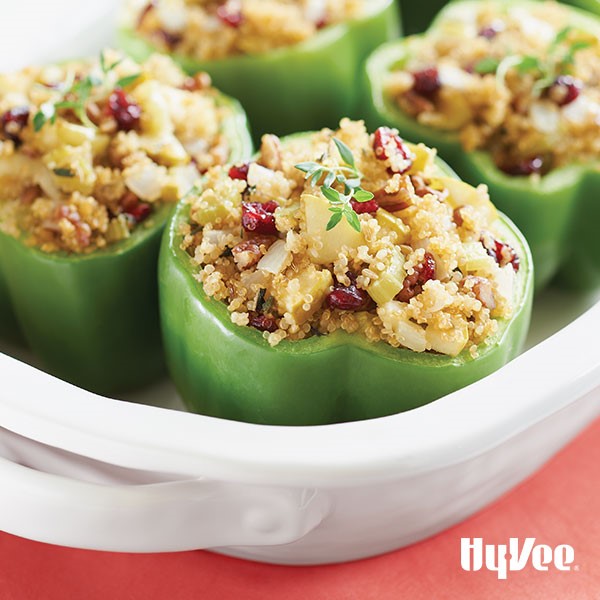 Green bell peppers in a casserole dish stuffed with quinoa, onions, celery, and dried cranberries garnished with thyme sprigs