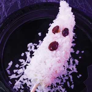 Frozen banana on a stick coated in white chocolate and shredded coconut and decorated with raisins