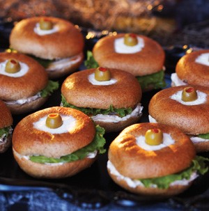 Tray of mini bagels filled with cream cheese, lunch meat, cheese and lettuce and topped with a pimento-stuffed olive