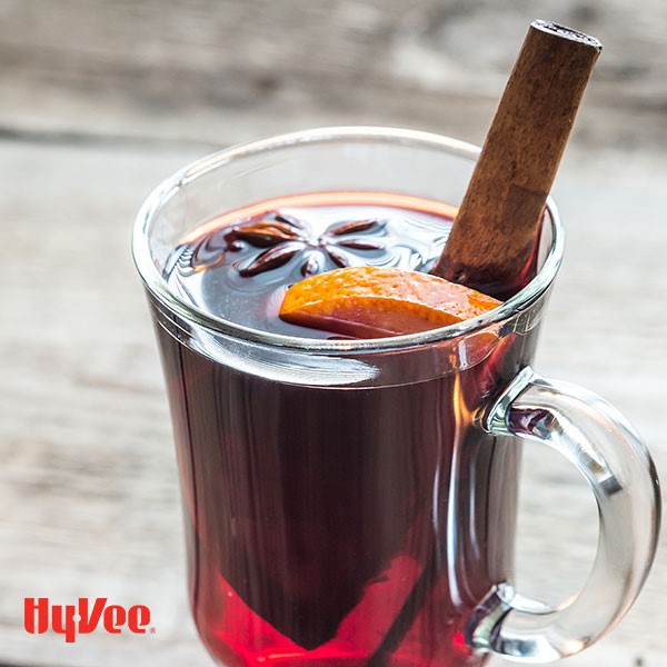 Glass clear mug filled with red mulled wine and garnished with whole star anise, cinnamon stick, and orange wedge