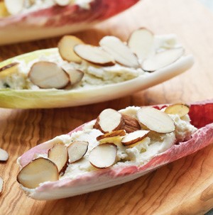 Belgian endive leaves filled with garlic and herb Boursin cheese and topped with sliced almonds on a wooden board