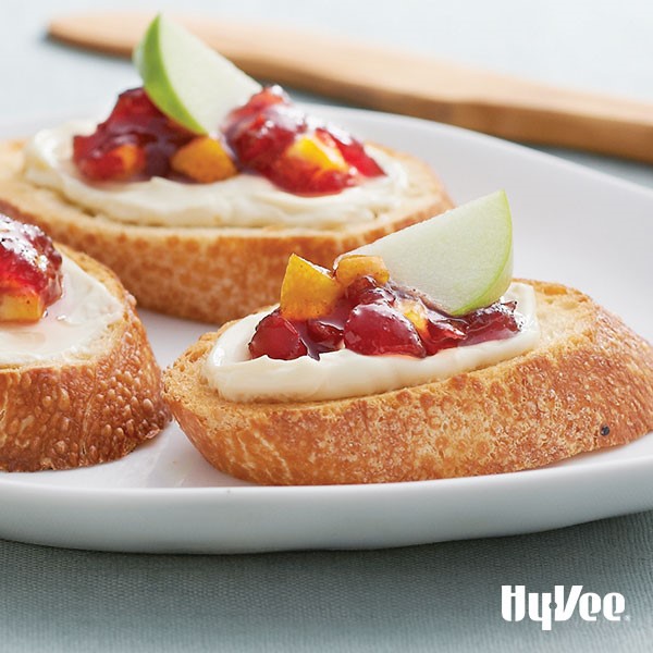 Plate of toasted baguettes topped with brie, cranberry relish, finely chopped orange and a green apple slice