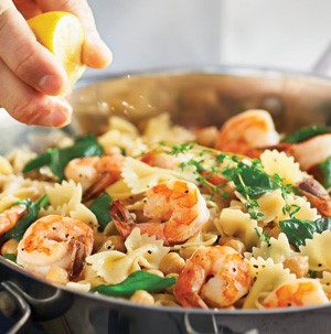Skillet filled with tail-on shrimp, bow tie pasta, and fresh greens for garnish
