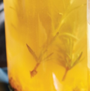 Glass filled with orange vinegar with fresh rosemary sprigs 