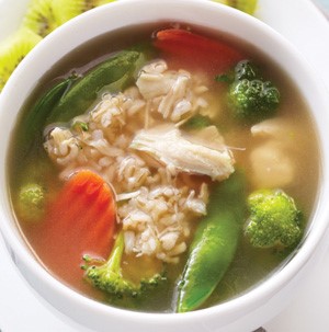 Soup in a bowl filled with broccoli, coined carrots, shredded chicken, and rice