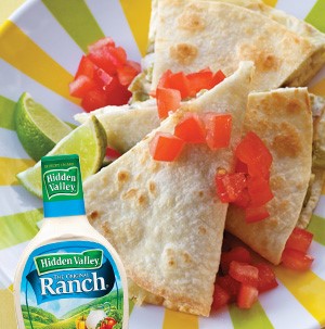 Quesadillas cut into wedge topped with fresh chopped tomatoes and lime wedges with bottle of ranch