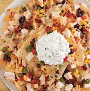 Tortilla chips topped with black beans, corn kernels, diced meat, chopped cooked bacon, and a dollop of sour cream on top