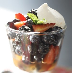 Glass of berry mixture topped with whipped cream and garnished with orange zest and fresh mint