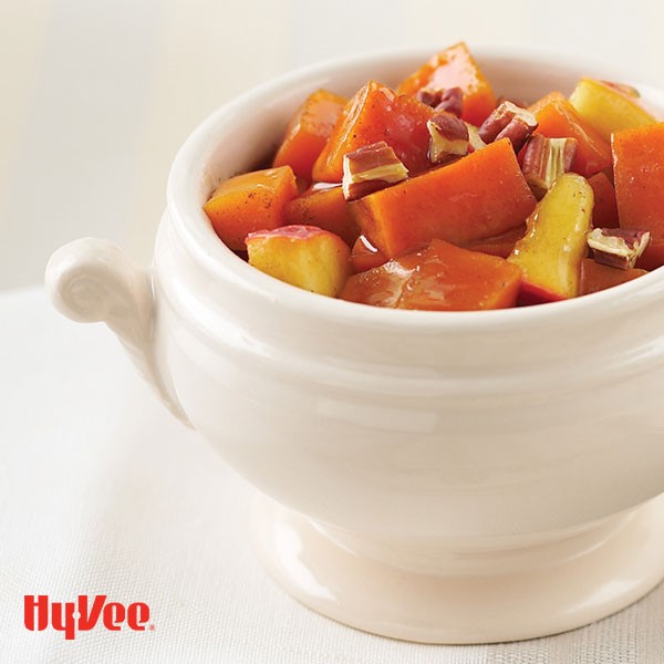 White dish filled with glazed sweet potatoes, apples, and chopped pecans