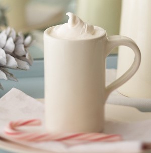 White mug topped with whipped cream and candy cane on the side