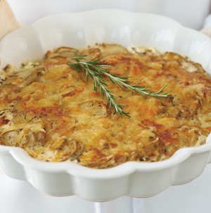 Cheesy potatoes in a scalloped white casserole dish garnished with fresh rosemary sprigs