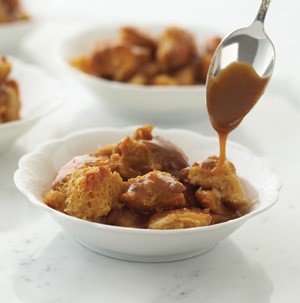 White bowl filled with bread pudding and drizzled with caramel sauce